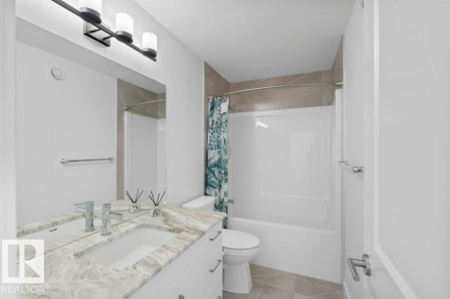 Bathroom featuring a white vanity with double sinks, a patterned stone countertop, and an integrated tub-shower combination with tiled surround - 19110 20A Avenue, Edmonton, AB - Indoor Photo Showing Bathroom