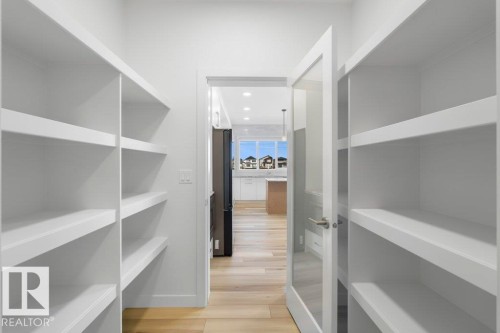 Walk-in pantry featuring extensive built-in shelving, white painted finishes, and wood-finish flooring - 19110 20A Avenue, Edmonton, AB - Indoor With Storage