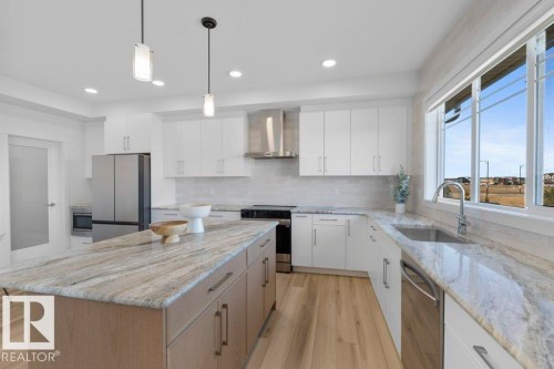 Bright kitchen featuring a central island with a light wood-finish base and a stone-finish countertop - 19110 20A Avenue, Edmonton, AB - Indoor Photo Showing Kitchen With Upgraded Kitchen