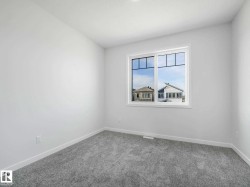 Bright room featuring a large window with multiple panes, light gray carpeting, crisp white walls, and matching white baseboards - 