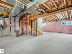 Unfinished basement featuring exposed wood joists, pink insulation, two windows, and a staircase - 
