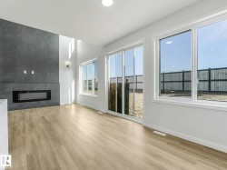 Spacious living area featuring a modern fireplace with a textured gray surround, high ceilings, large windows, a glass sliding door, and light wood-finish flooring - 