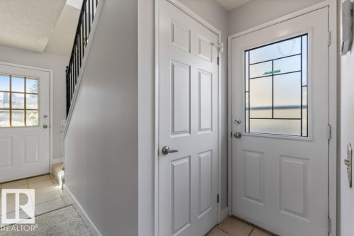Entryway featuring a white paneled door with decorative glass, tiled flooring, and a staircase with black iron balusters - 3736 12 Avenue, Edmonton, AB - Indoor Photo Showing Other Room