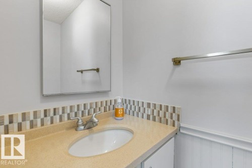 Bathroom vanity featuring a light-toned countertop with integrated sink, mosaic tile backsplash, and brushed nickel faucet - 3736 12 Avenue, Edmonton, AB - Indoor Photo Showing Bathroom