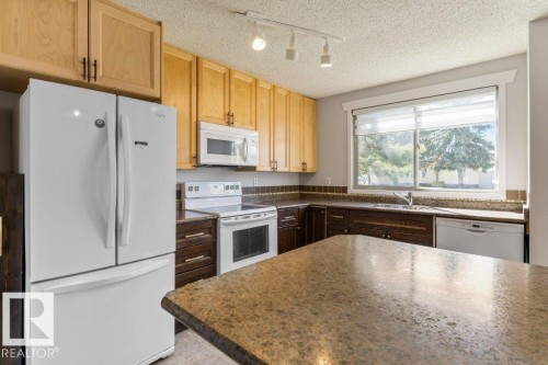 Kitchen featuring a large window, dual-tone cabinetry, stone-finish countertops, and a full suite of white appliances - 3736 12 Avenue, Edmonton, AB - Indoor Photo Showing Kitchen