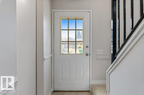 Entryway featuring a white paneled door with divided lite window, light-colored tile flooring, and a carpeted staircase with dark balusters - 3736 12 Avenue, Edmonton, AB - Indoor Photo Showing Other Room