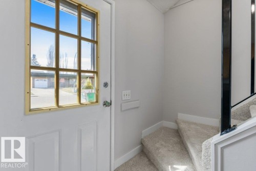 Entry door with a grid-pattern glass insert and brass-tone framing, complemented by light grey carpeting on the adjacent staircase featuring a dark-toned railing - 3736 12 Avenue, Edmonton, AB - Indoor Photo Showing Other Room