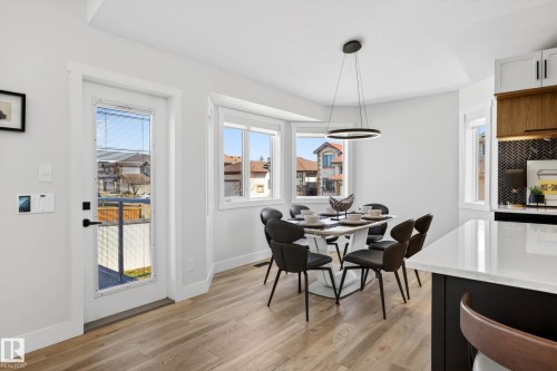 Bright dining area featuring light wood-finish flooring, a contemporary chandelier, a full-lite exterior door, and a bay window - 324 Cutts Crest, Edmonton, AB - Indoor Photo Showing Dining Room