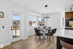 Bright dining area featuring light wood-finish flooring, a contemporary chandelier, a full-lite exterior door, and a bay window - 
