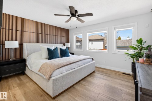Bedroom featuring a wood-slat accent wall, three windows, and wood-finish flooring - 324 Cutts Crest, Edmonton, AB - Indoor Photo Showing Bedroom