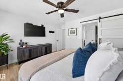 Bedroom featuring wood-finish flooring, a ceiling fan with integrated lighting, a wall-mounted flat-screen television, a wooden media console, and a contemporary barn door - 