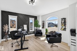Room featuring a dark accent wall with geometric paneling, light wood-finish flooring, and a modern chandelier - 