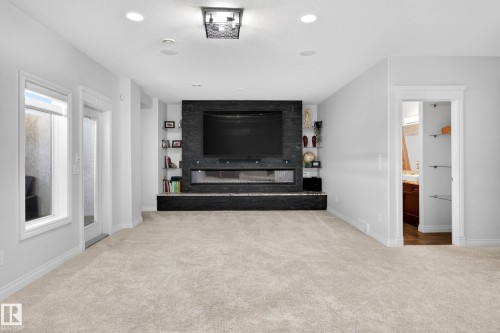 Carpeted living area featuring a built-in entertainment center with a dark stone-finish surround, an electric fireplace, and integrated shelving - 324 Cutts Crest, Edmonton, AB - Indoor