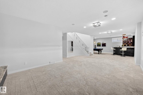 Spacious recreation room featuring light-toned carpeting, recessed lighting, a staircase with decorative iron balusters, a built-in wet bar with dark stone-look facing, and a pool table area - 324 Cutts Crest, Edmonton, AB - Indoor Photo Showing Other Room