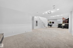 Spacious recreation room featuring light-toned carpeting, recessed lighting, a staircase with decorative iron balusters, a built-in wet bar with dark stone-look facing, and a pool table area - 