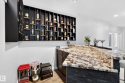 Built-in bar featuring a dark wood-finish base cabinet, a natural stone countertop, a stone veneer bar front, an integrated sink, and an illuminated display shelving system - 