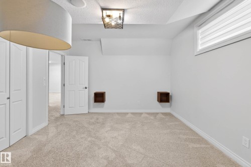 Plush carpeted room featuring white walls and trim, a horizontal window with blinds, and two dark wood-finish floating wall shelves - 324 Cutts Crest, Edmonton, AB - Indoor Photo Showing Other Room