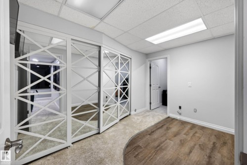 Mirrored sliding closet doors with decorative white framing, wood-finish flooring, and a drop ceiling with recessed lighting - 324 Cutts Crest, Edmonton, AB - Indoor Photo Showing Other Room