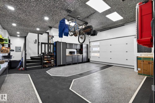 Garage featuring gray speckled epoxy flooring with black and white accents, a modern white garage door with clear glass inserts, built-in cabinetry, recessed lighting, and a textured ceiling - 324 Cutts Crest, Edmonton, AB - Indoor Photo Showing Garage