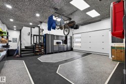 Garage featuring gray speckled epoxy flooring with black and white accents, a modern white garage door with clear glass inserts, built-in cabinetry, recessed lighting, and a textured ceiling - 