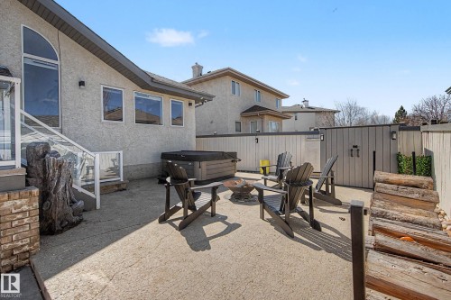 Concrete patio area featuring a hot tub, fire pit, privacy fencing, and exterior lighting - 324 Cutts Crest, Edmonton, AB - Outdoor With Deck Patio Veranda With Exterior