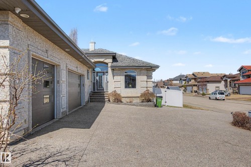 Multi-car garage with contemporary doors, a light-colored stucco exterior, arched window details, a prominent chimney, and a concrete driveway - 324 Cutts Crest, Edmonton, AB - Outdoor