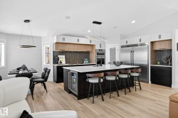 Spacious kitchen featuring a large island with seating, a built-in beverage cooler, stainless steel appliances, a herringbone tile backsplash, and light wood-finish flooring - 