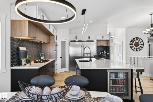 Spacious kitchen featuring a large island with sink, integrated beverage cooler, stainless steel appliances, herringbone tile backsplash, and light wood-finish flooring - 324 Cutts Crest, Edmonton, AB - Indoor