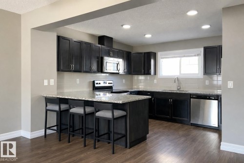 Kitchen featuring dark cabinetry with brushed nickel hardware, light granite countertops, and a subway tile backsplash - 1520 105 Street, Edmonton, AB - Indoor Photo Showing Kitchen With Upgraded Kitchen