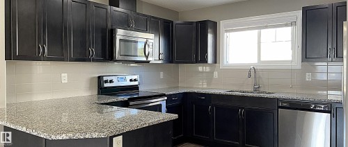 Kitchen featuring dark wood-finish cabinetry, speckled countertops, stainless steel appliances, a tile backsplash, and a window with white trim - 1520 105 Street, Edmonton, AB - Indoor Photo Showing Kitchen With Upgraded Kitchen
