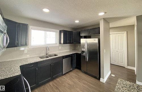 Modern kitchen featuring dark cabinetry, light-toned granite-style countertops, stainless steel appliances, and wood-finish flooring - 1520 105 Street, Edmonton, AB - Indoor Photo Showing Kitchen With Double Sink