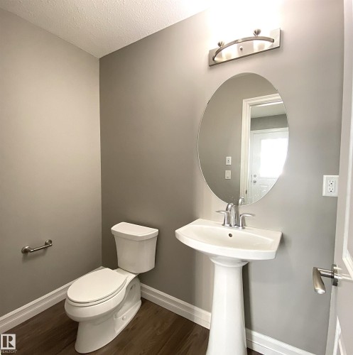 Powder room featuring a pedestal sink with chrome faucet, oval mirror, and overhead vanity lighting - 1520 105 Street, Edmonton, AB - Indoor Photo Showing Bathroom