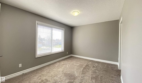 Neutral-toned room featuring a window with horizontal blinds, textured carpet flooring, white baseboards, and a flush-mount ceiling light fixture - 1520 105 Street, Edmonton, AB - Indoor Photo Showing Other Room
