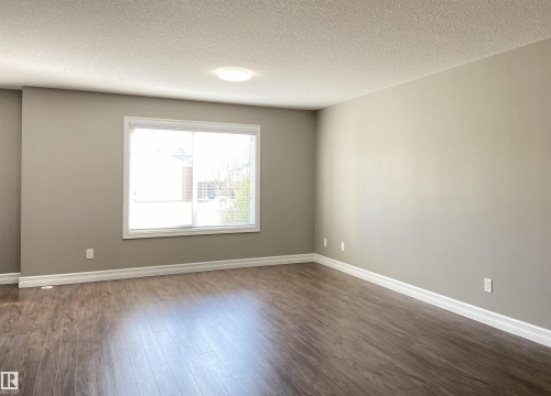 Spacious room featuring wood-finish flooring, neutral wall paint, white baseboards, and a large window with white blinds - 1520 105 Street, Edmonton, AB - Indoor Photo Showing Other Room
