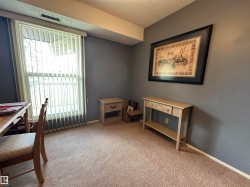 Carpeted room featuring a large window with vertical blinds, painted walls, and a ceiling-mounted air vent - 