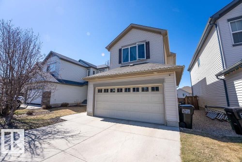 Two-story residence featuring light-colored siding, an attached garage with a panel door and upper window inserts, a concrete driveway, and dark-colored roof shingles - 1734 63A Street, Edmonton, AB - Outdoor With Exterior