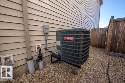 Exterior mechanical unit on a gravel bed, featuring tan horizontal siding and a wooden privacy fence - 1734 63A Street, Edmonton, AB - Outdoor With Exterior