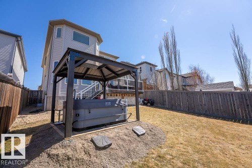 Backyard featuring a hot tub under a dark-framed gazebo, a multi-level deck with white lattice skirting, and an expansive lawn area - 1734 63A Street, Edmonton, AB - Outdoor