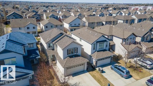 Contemporary two-story residence featuring a front-facing attached garage, stone accents on the garage facade, light-colored siding, dark trim, and a shingled roof - 1734 63A Street, Edmonton, AB - Outdoor With Facade