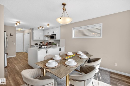Open-concept dining area featuring a modern light fixture, wood-finish flooring, and direct access to a contemporary kitchen with white cabinetry and an island - 7723 7A Avenue, Edmonton, AB - Indoor Photo Showing Dining Room