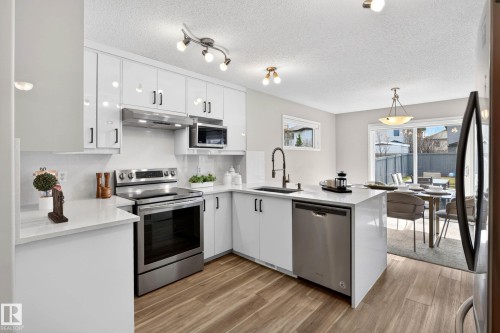 Modern kitchen featuring high-gloss white cabinetry, stainless steel appliances, and wood-finish flooring - 7723 7A Avenue, Edmonton, AB - Indoor Photo Showing Kitchen