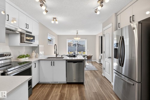 Modern kitchen featuring white cabinetry, stainless steel appliances, wood-finish flooring, and light-toned countertops - 7723 7A Avenue, Edmonton, AB - Indoor Photo Showing Kitchen With Upgraded Kitchen