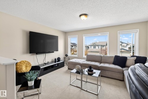 Carpeted living area featuring multiple large windows, a ceiling-mounted light fixture, and a built-in entertainment console - 7723 7A Avenue, Edmonton, AB - Indoor Photo Showing Living Room