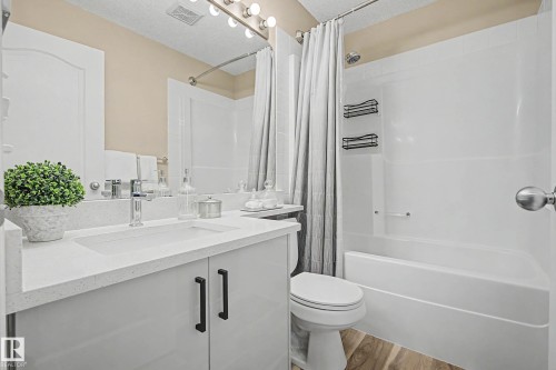 Bathroom featuring a white vanity with a rectangular integrated sink, chrome faucet, and dark cabinet pulls - 7723 7A Avenue, Edmonton, AB - Indoor Photo Showing Bathroom