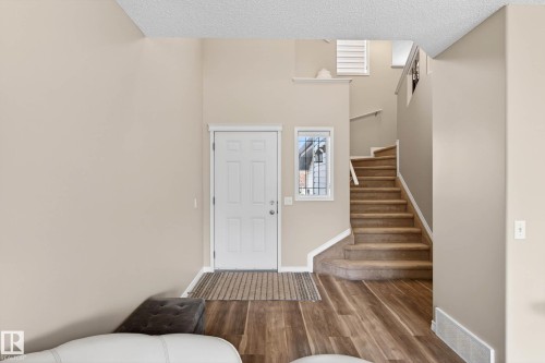 Entryway featuring a paneled door with an adjacent sidelight window, wood-finish flooring, and a carpeted staircase with white trim - 7723 7A Avenue, Edmonton, AB - Indoor Photo Showing Other Room