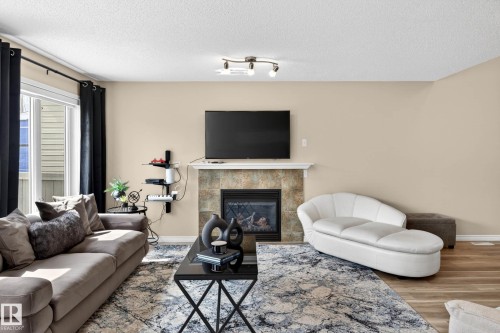 Living area featuring a tiled fireplace with mantel, built-in electric insert, and a large window with vertical blinds - 7723 7A Avenue, Edmonton, AB - Indoor Photo Showing Living Room With Fireplace