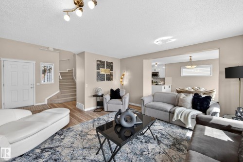 Open-concept living area featuring wood-finish flooring, a contemporary overhead light fixture, and a neutral color palette - 7723 7A Avenue, Edmonton, AB - Indoor Photo Showing Living Room