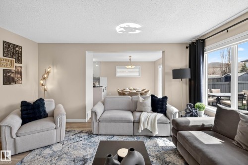 Spacious living area featuring light neutral wall paint, wood-finish flooring, and a large window with exterior backyard access - 7723 7A Avenue, Edmonton, AB - Indoor Photo Showing Living Room