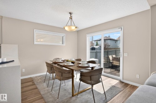 Dining area featuring wood-finish flooring, a contemporary chandelier, a horizontal window with horizontal blinds, and a sliding glass door providing exterior access - 7723 7A Avenue, Edmonton, AB - Indoor Photo Showing Dining Room