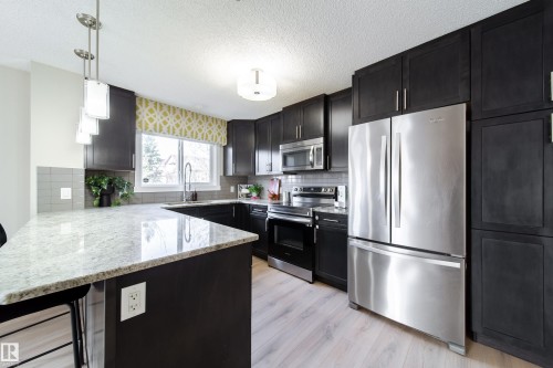 Kitchen featuring dark cabinetry, stainless steel appliances, light granite countertops, a tiled backsplash, and wood-finish flooring - 117 2229 44 Avenue, Edmonton, AB - Indoor Photo Showing Kitchen With Stainless Steel Kitchen With Upgraded Kitchen